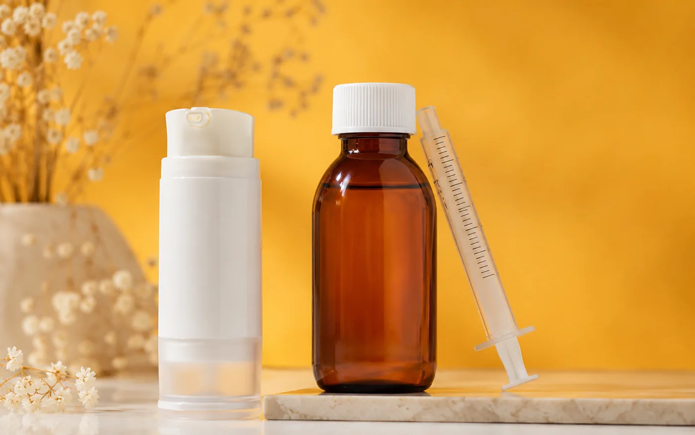 Transdermal gel applicator, amber oral suspension bottle, and dosing syringe against a golden background